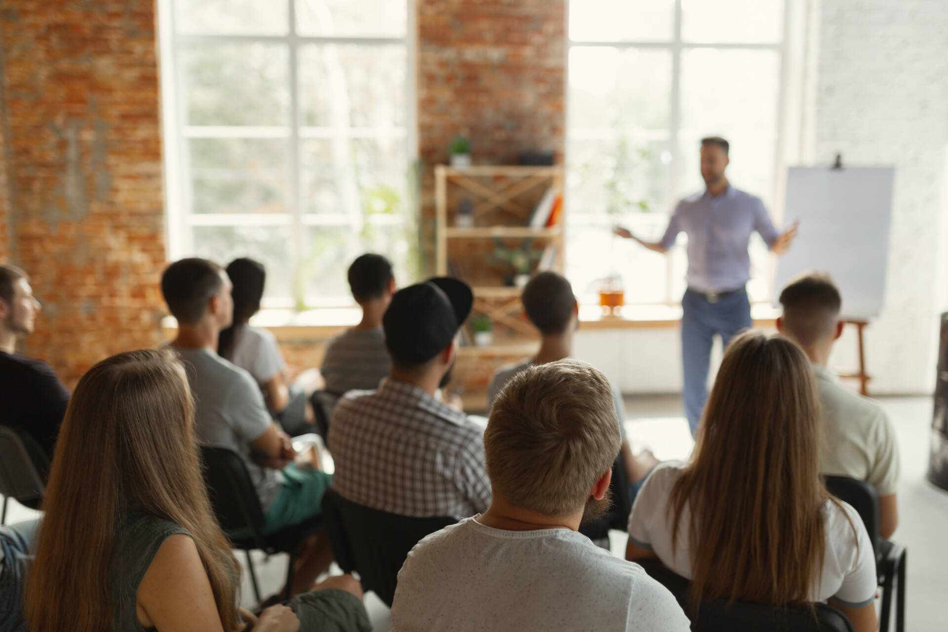 Male speaker giving presentation in hall at university workshop. Audience or conference hall. Rear view of unrecognized participants in audience. Scientific conference event, training. Education concept.